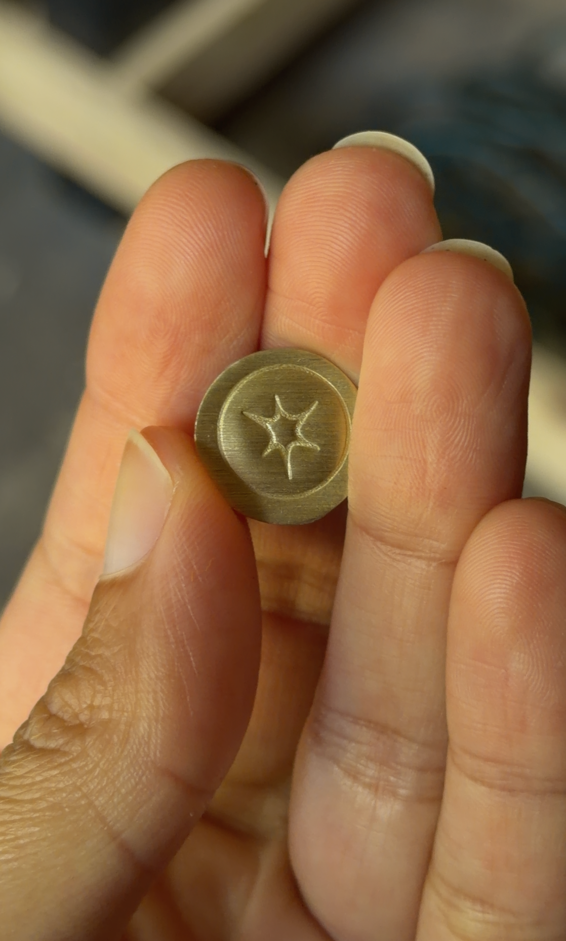 A close-up of a hand holding a small round brass button with a starburst design in the center.